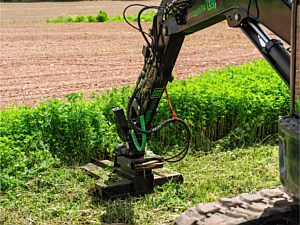 Brush mower on an excavator being used to mow a ditch on the side of a driveway